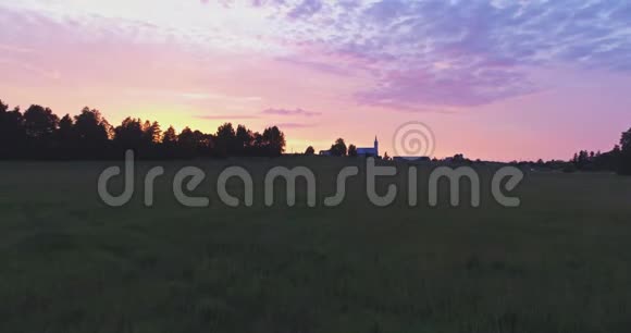 令人惊叹的美丽日落鸟瞰小乡村小镇绿色的田野和高大的树木视频的预览图