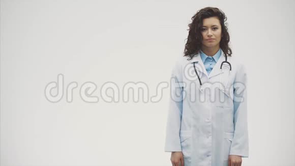 幸福的年轻微笑女孩医生的肖像穿着白色长袍双手交叉站在灰色的视频的预览图