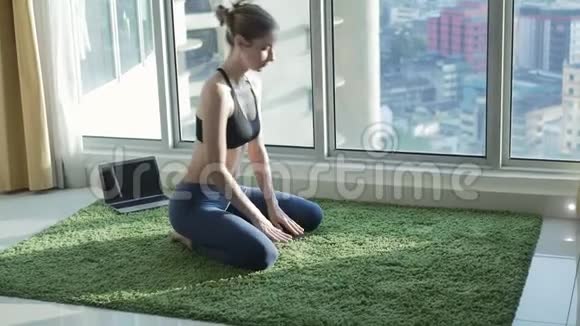 有城市景观背景的年轻女性在家练习瑜伽视频的预览图
