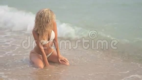年轻漂亮的晒黑女孩穿着比基尼金发坐在海边的日落视频的预览图