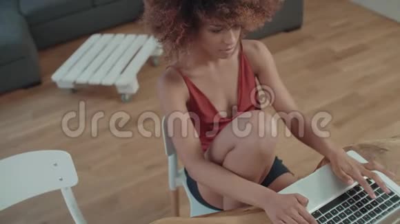 年轻的美国黑人妇女坐在桌旁使用笔记本电脑视频的预览图
