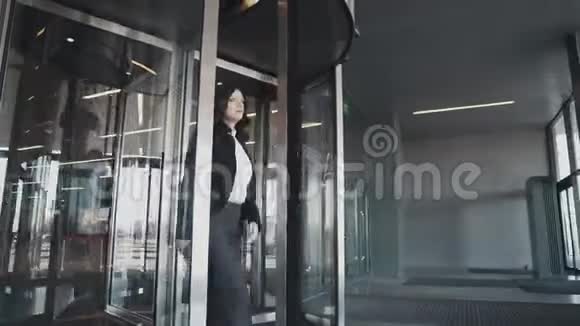 一个女商人从一个现代商业中心的旋转门离开穿西装的女孩看手表视频的预览图
