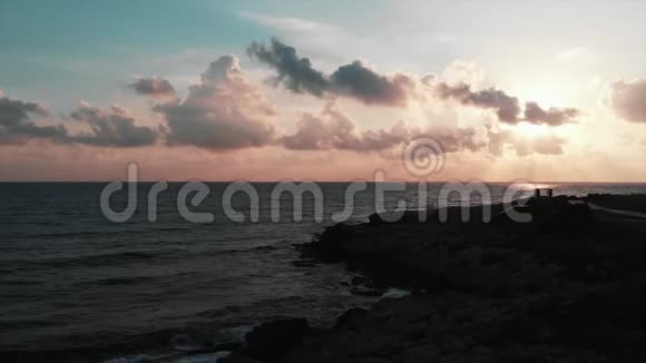 带海洋和岩石海滩的美丽粉红色日落的空中景色视频的预览图