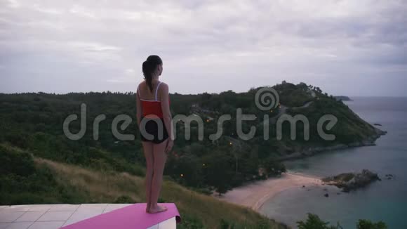 女人在高处练习瑜伽健身运动日出时可以看到令人惊叹的岛屿景观视频的预览图