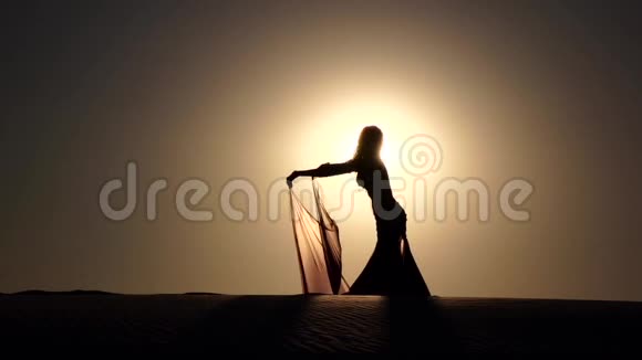 手里拿着面纱的女孩在海滩上跳舞肚皮舞剪影慢动作视频的预览图