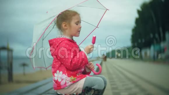 小女孩带着雨伞在雨中玩耍在海岸吃冰淇淋视频的预览图