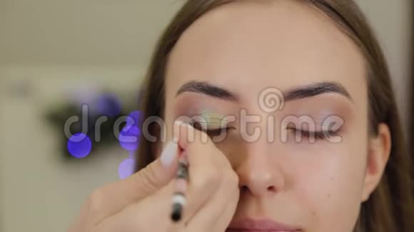 专业的眼妆发型师化妆师将化妆应用于一个年轻的女人在美容院有一个特殊的刷子视频的预览图