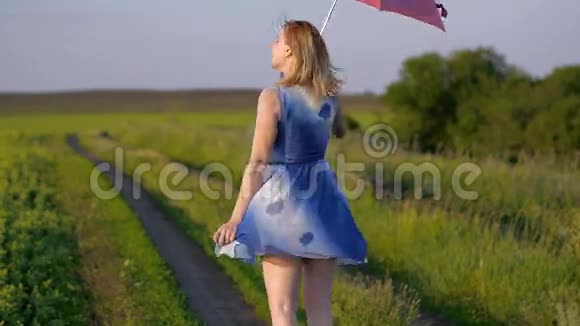 一个美丽的女孩带着红伞在夕阳下微笑的情感绿色草地上微笑的女孩跳舞的肖像视频的预览图