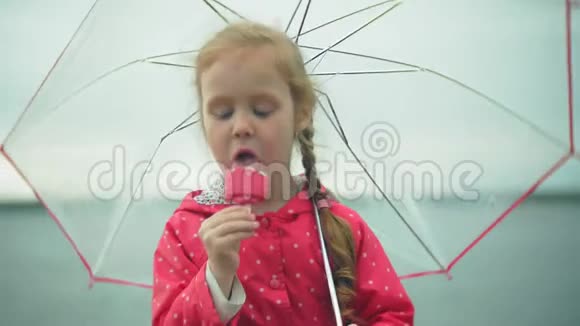 小女孩带着雨伞在雨中玩耍在海岸吃冰淇淋视频的预览图