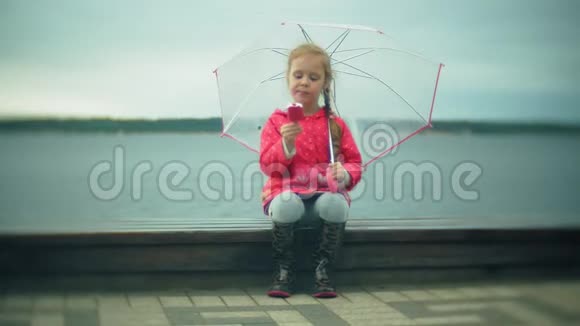 小女孩带着雨伞在雨中玩耍在海岸吃冰淇淋视频的预览图