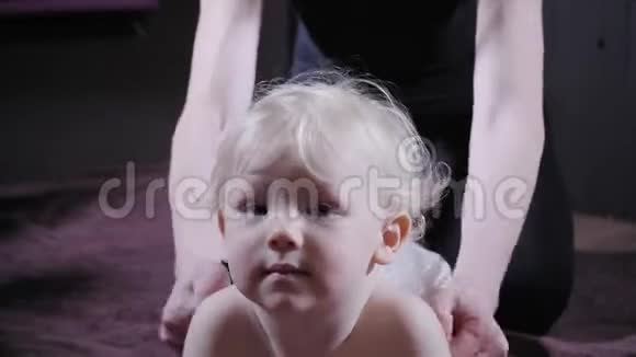 婴儿按摩妈妈或治疗师在家给宝宝做按摩保健和医药理念金发男孩视频的预览图
