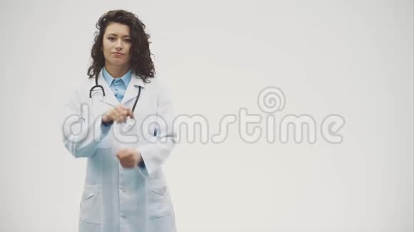 幸福的年轻微笑女孩医生的肖像穿着白色长袍双手交叉站在灰色的视频的预览图