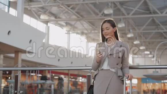 快乐的年轻女人在购物中心使用智能手机在机场候机楼里有智能手机的女商人自由职业者视频的预览图