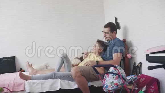 一个年轻的父亲和他的小女儿在一起爸爸和孩子在家坐在床上玩亲子视频的预览图