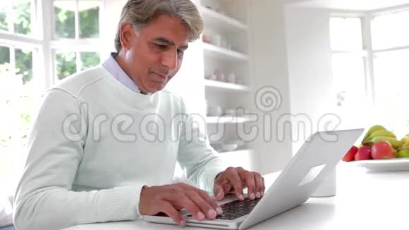 印度男人在家庭厨房里使用笔记本电脑视频的预览图