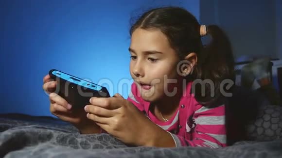 十几岁的小女孩在网上玩便携式电子游戏晚上在室内玩游戏机视频的预览图