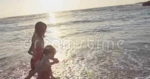 日落时三个孩子在海滩上奔跑的照片视频的预览图
