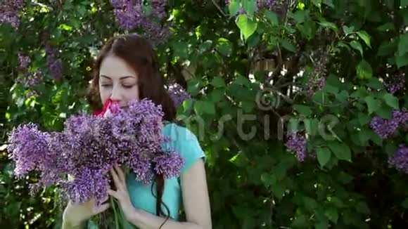 美丽的女人在春天公园散步带着一束紫丁香视频的预览图