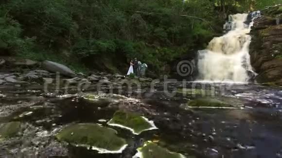 年轻的新婚夫妇走在瀑布附近视频的预览图
