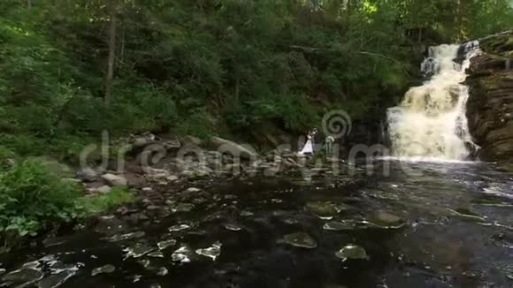 年轻的新婚夫妇走在瀑布附近视频的预览图