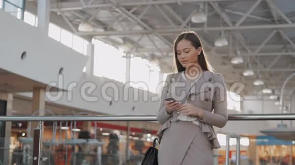 快乐的年轻女人在购物中心使用智能手机在机场候机楼里有智能手机的女商人自由职业者视频的预览图
