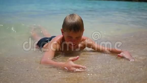 孩子躺在沙滩上在阳光明媚的日子里在海浪中游泳视频的预览图