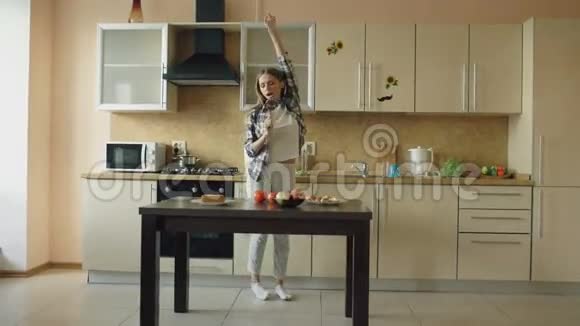在家厨房做饭的时候一个快乐的年轻风趣的女人一边用勺子跳舞一边唱歌视频的预览图