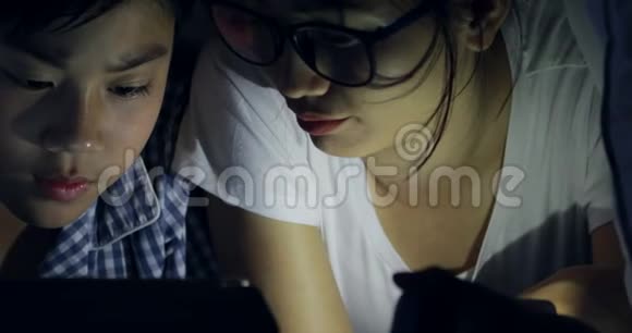 亚洲家庭的年轻母亲儿子在床上玩手机或智能手机夜晚视频的预览图