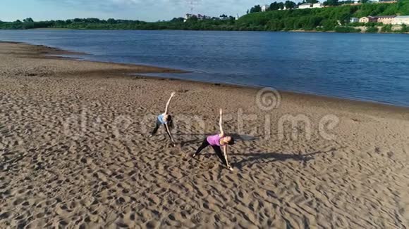 两个女人在城市河边的沙滩上做瑜伽日出时美丽的城市景色视频的预览图