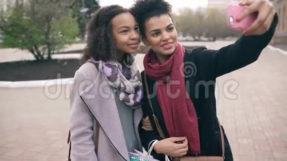 两个可爱的非裔美国女人带着购物袋和微笑自拍朋友们在参观商场销售后玩得很开心视频的预览图