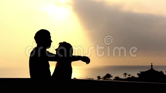 日落阳台上一对爱的情侣在海边拥抱和亲吻的剪影视频的预览图