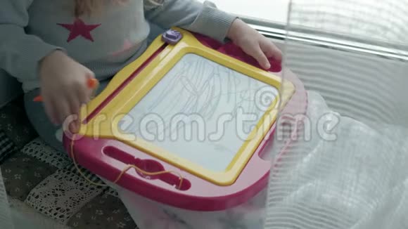 一个红色波浪发的小女孩坐在窗台上画在一块磁性的木板上教育的概念视频的预览图