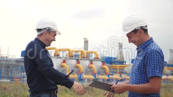 团队合作工业煤气生产站的概念慢动作视频两名戴头盔的工程师在煤气上握手视频的预览图