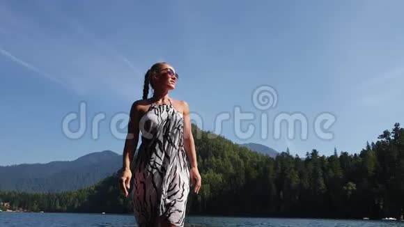 女人戴着太阳镜和一条薄纱披肩在码头上水上行走女孩在洪水木水下码头休息人行道视频的预览图