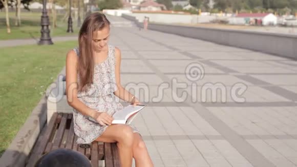 坐在长凳上拿书的年轻女子视频的预览图