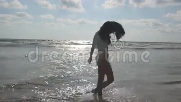 穿着比基尼和衬衫的快乐女人在海滩上的海水边散步年轻漂亮的女孩享受生活和乐趣视频的预览图