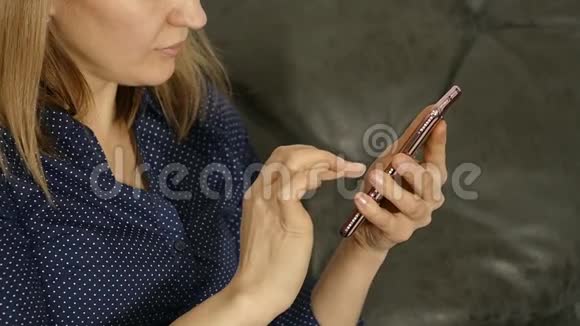 金发女人坐在沙发上用智能手机视频的预览图