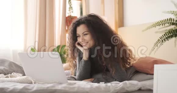 快乐的女人在家里的床上使用笔记本电脑视频的预览图