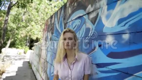 年轻的金发女孩在墙的背景上摆着涂鸦视频的预览图