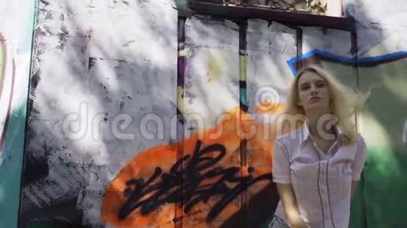 年轻的金发女孩在墙的背景上摆着涂鸦视频的预览图