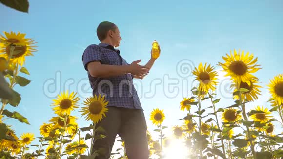农夫穿着格子衬衫手里拿着一个塑料瓶向日葵油站在田野里缓慢的生活方式视频的预览图