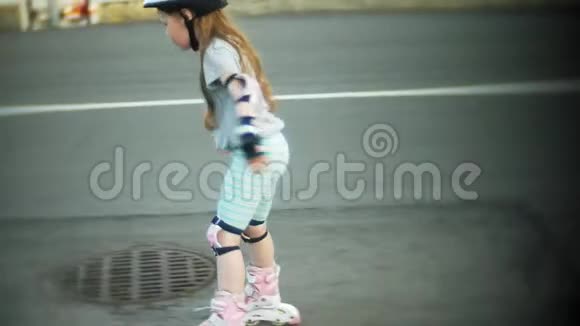 一个戴着头盔的小女孩和穿着溜冰鞋的防守冰鞋这孩子在公园里的滚筒上滚动女孩学习视频的预览图