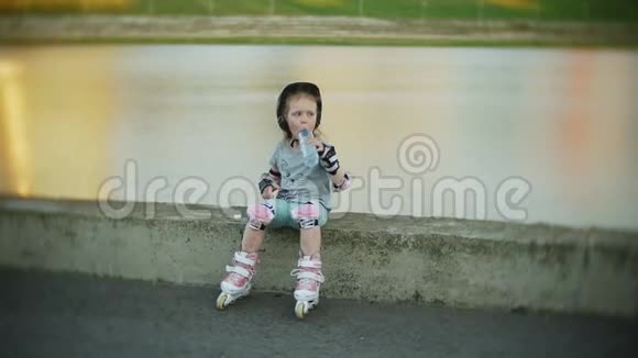 一个戴着头盔的小女孩和穿着溜冰鞋的防守冰鞋这孩子在公园里的滚筒上滚动女孩学习视频的预览图