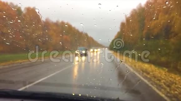汽车行驶在路上秋天美丽的风景林雨滴在玻璃车上模糊的背景慢动作视频的预览图