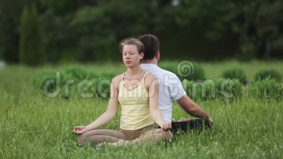 一男一女静心极乐年轻的瑜伽教练在绿草如茵的城市公园练习成功的青年视频的预览图