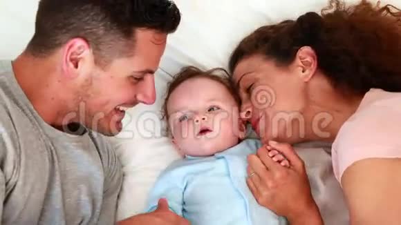 穿着蓝色婴儿裤的小男孩和快乐的父母在床上视频的预览图