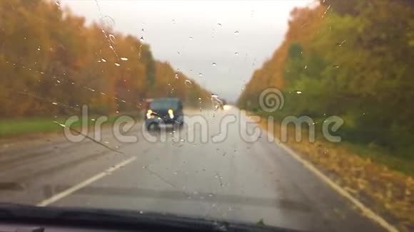 汽车行驶在路上秋天美丽的风景林雨滴在玻璃车上模糊的旅行背景缓慢视频的预览图