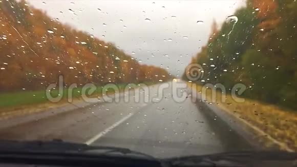 汽车行驶在路上秋天旅行美丽的风景林雨滴在玻璃车上模糊的背景缓慢视频的预览图