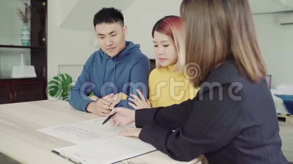 快乐的年轻亚洲夫妇和房地产经纪人一位性格开朗的年轻人和妻子一起坐在办公桌前签署一些文件视频的预览图