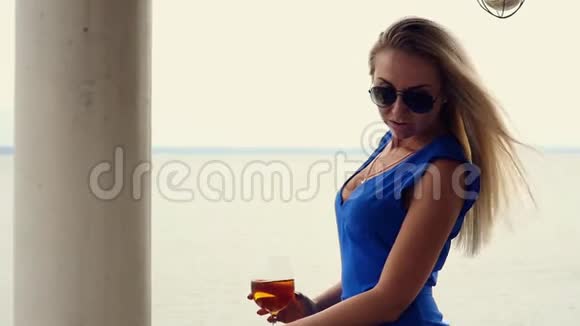 美丽的金发碧眼的金发碧眼正在喝着酒杯里的白葡萄酒欣赏着海洋的地平线站在阳台上视频的预览图